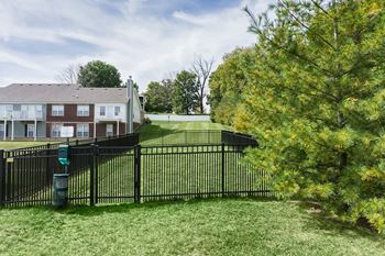 A black fence surrounds a green lawn in front of a brick building.